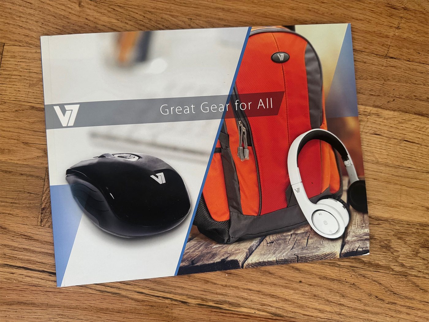 Printed V7 catalog cover reading Great Gear for All, showing a wireless mouse, headphones and an orange backpack